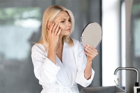 Moteris, besitikrinanti veidą veidrodyje