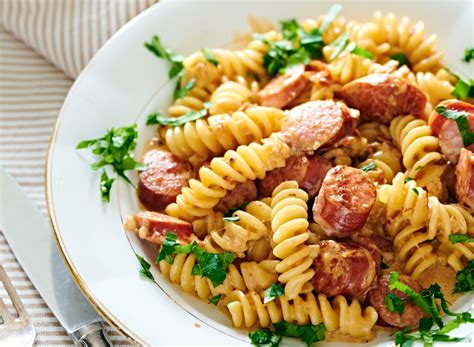 Lėkštė makaronų su rūkytomis dešrelėmis ir kreminiu padažu, pabarstyta žolelėmis