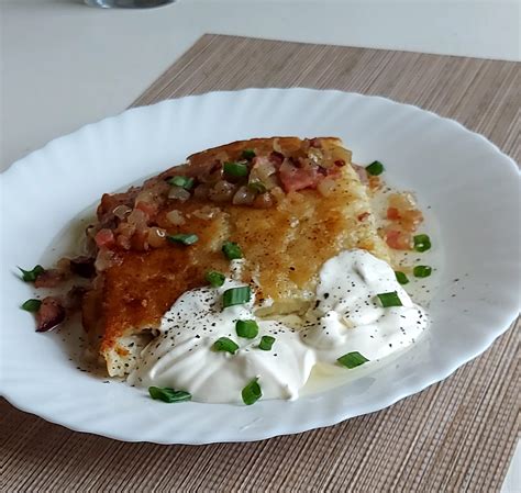 Vaizdas su šviežiai keptais varškėčiais ant lėkštės, papuoštais uogomis ir grietine.