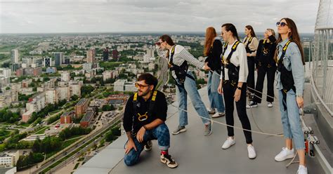 Žmonės vaikštantys TV bokšto kraštu su saugos įranga