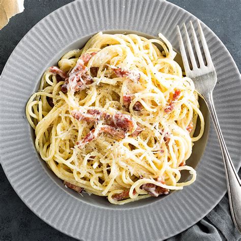 Šviežiai paruoštų Spagečių Carbonara lėkštė su tarkuotu sūriu ir juodaisiais pipirais